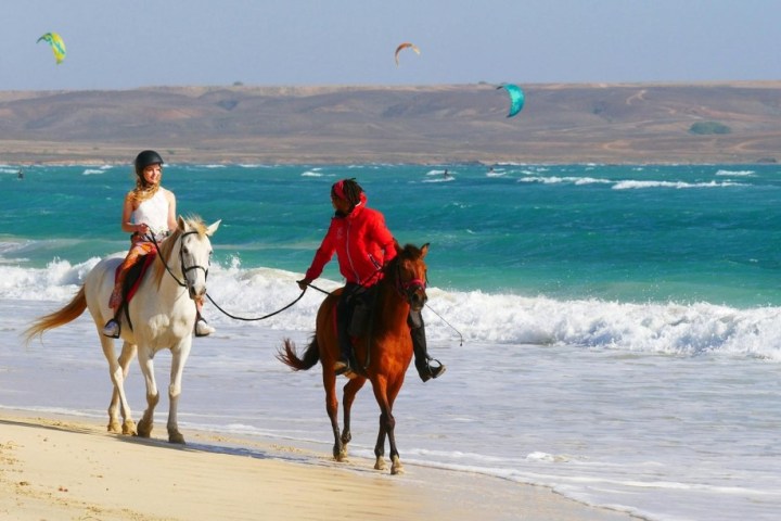 a group of people riding horses on a beach
