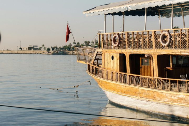 Wooden boat with canopy and flag docked on calm water, clear sky.