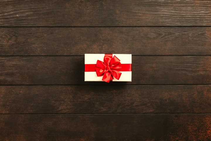 Gift box with red ribbon on dark wooden background.