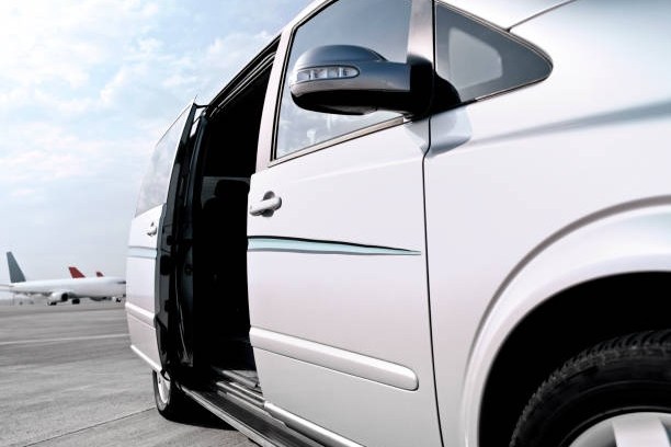 White van with open sliding door on runway near airplanes.