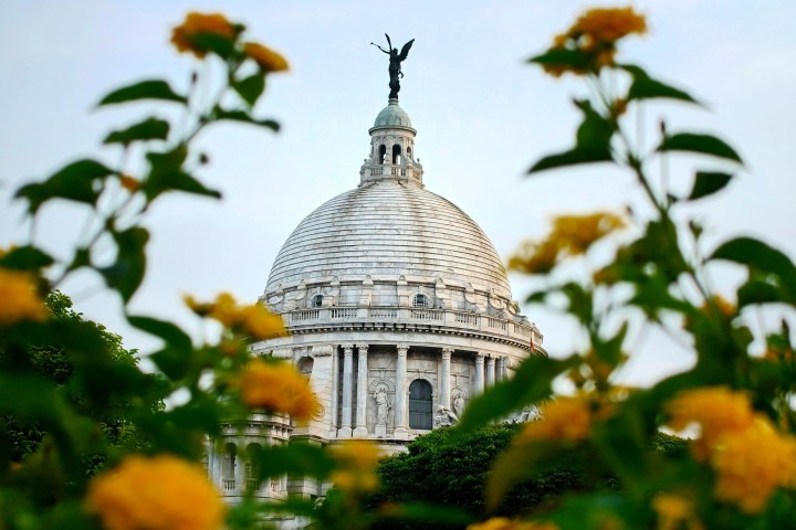 White dome building with statue on top, framed by yellow flowers and green leaves.