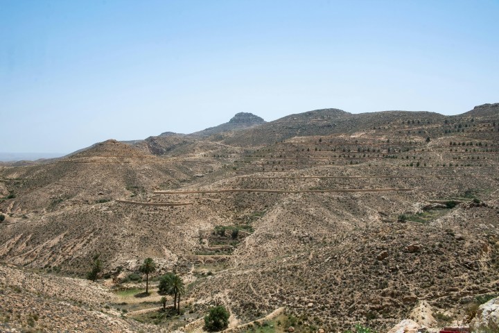 Arid landscape with terraced hills and sparse vegetation under a clear blue sky.