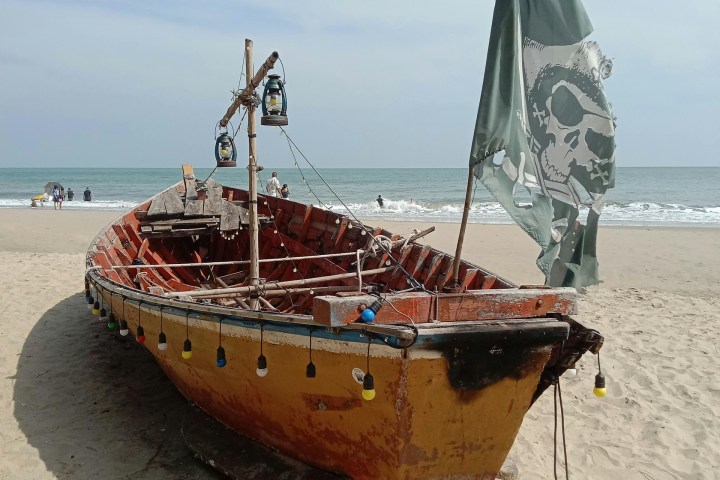 Old boat with pirate flag on a sandy beach near the ocean.