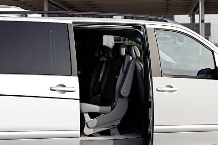 Open white minivan door near international terminal entrance.
