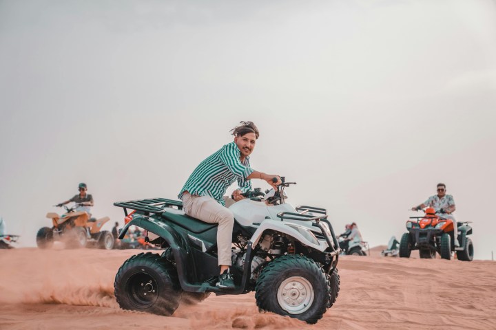 People riding ATVs on sand dunes under a cloudy sky.
