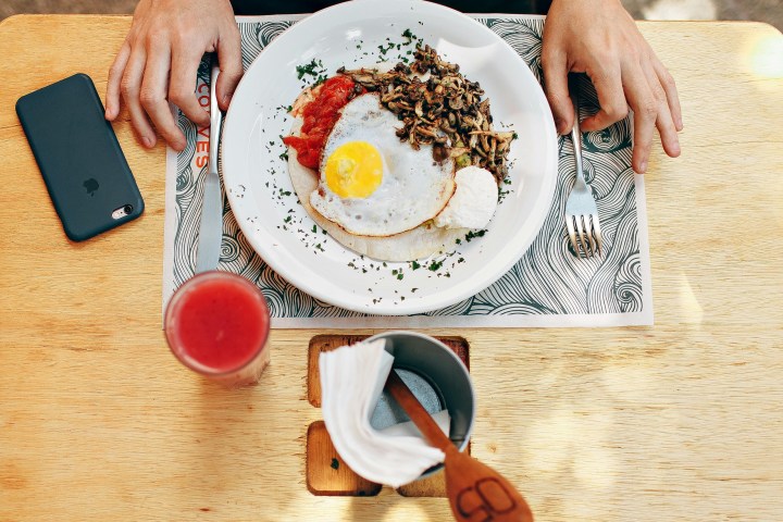 Plate with a fried egg, mushrooms, and sauce on a table with a phone and drink.