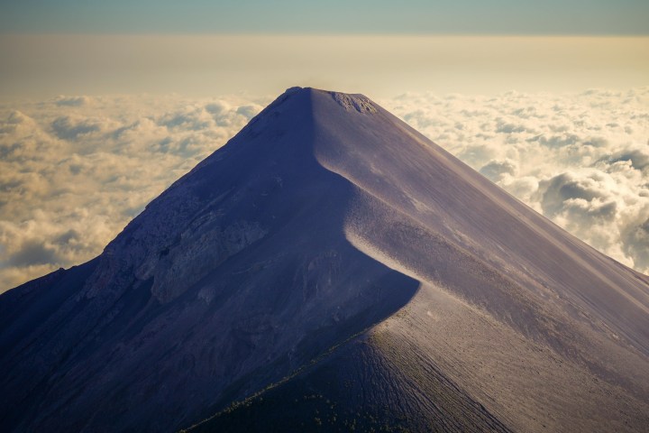 A mountain peak above the clouds under a clear sky.