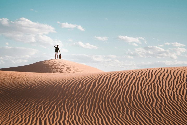 Person standing on sand dune under a blue sky with scattered clouds.