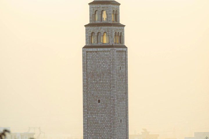 Tall stone tower with arched windows against a hazy sky and urban landscape.